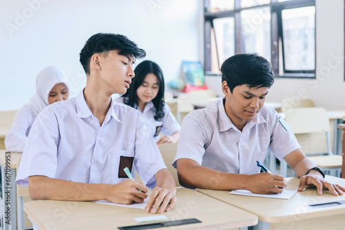 Foto Young Asian student in school uniform cheating to classmate during exam in schoo