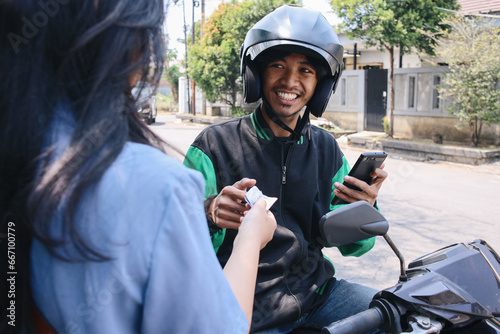 Cheerful online motorcycle taxi driver receiving cash money payment from female customer  photo