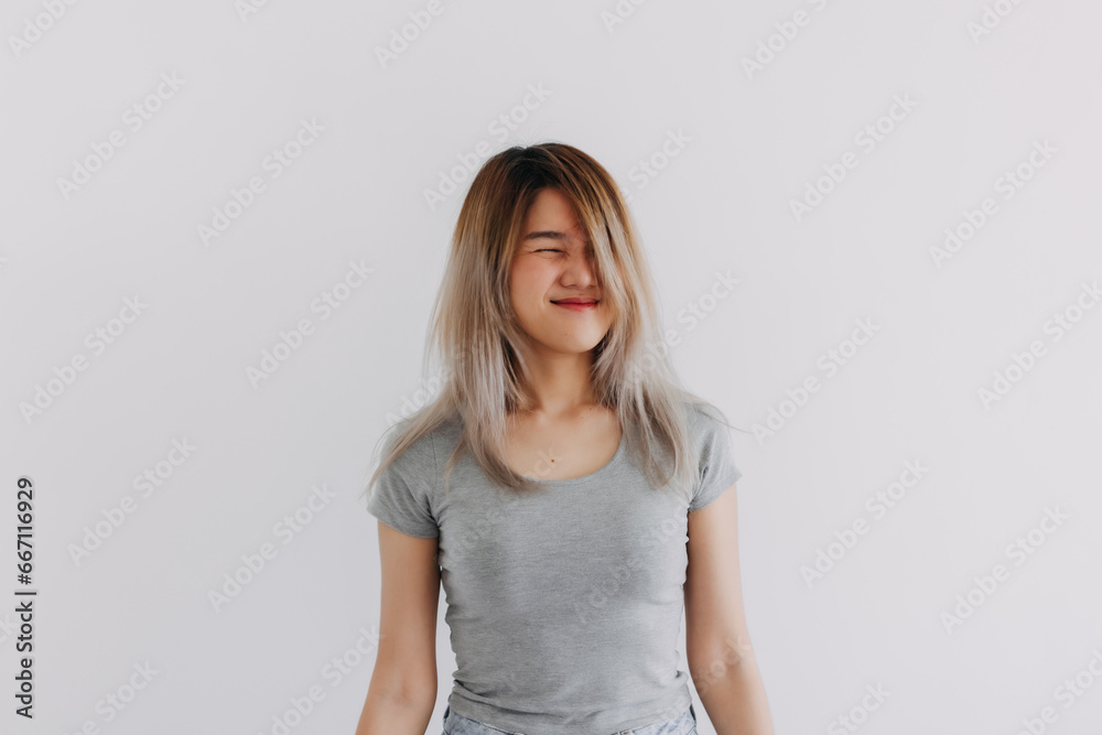 Asian Thai woman wear grey, keep straight smiling face, look inscrutable with messy hair, thinking something while standing and closing eyes, isolated on white background wall. Asian Thai woman wear grey, keep straight smiling face, look inscrutable with messy hair, thinking something while standing and closing eyes, isolated on white background wall.