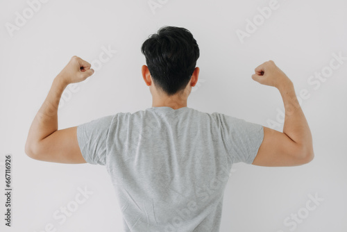 Backside view of Asian man back wear grey t-shirt raising arms, showing muscles biceps power, healthy body builder isolated over white background wall.