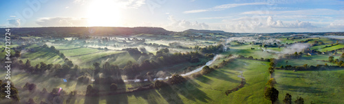 Aerial panorama picture of the river Otter near Honiton and Ottery St Mary. Sunrise and rolling mist cross the lush green fields below. Spectacular landscape. 