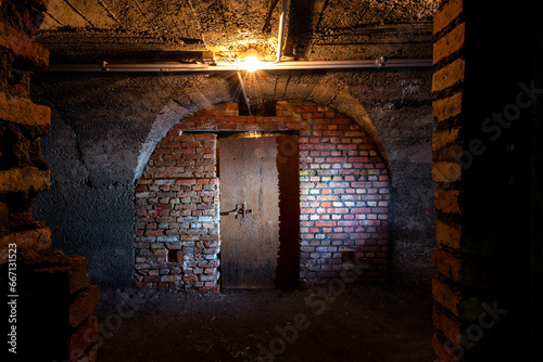 Historic bunker tunnel from world war 2 built with reinforced concrete now is a scary lost place in the dark with wet walls and a spooky rusty iron door. Light bulb illuminating an old brick wall. 