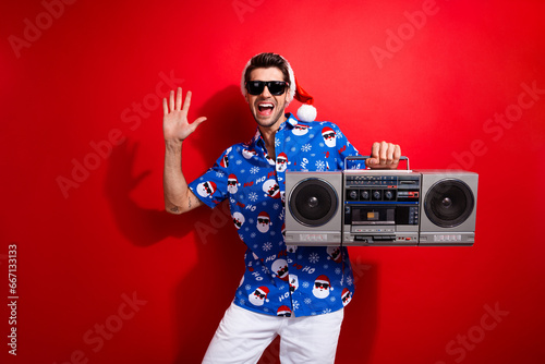 Photo of young positive guy wear cool sunglasses macho listen vintage cassette player raised palm up isolated on red color background