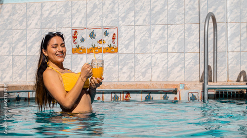 Mujer con bikini caliente atractiva sonriente sosteniendo un vaso en su mano durante un baño en la piscina , tomando sol, verano, teléfono celular,vaciones