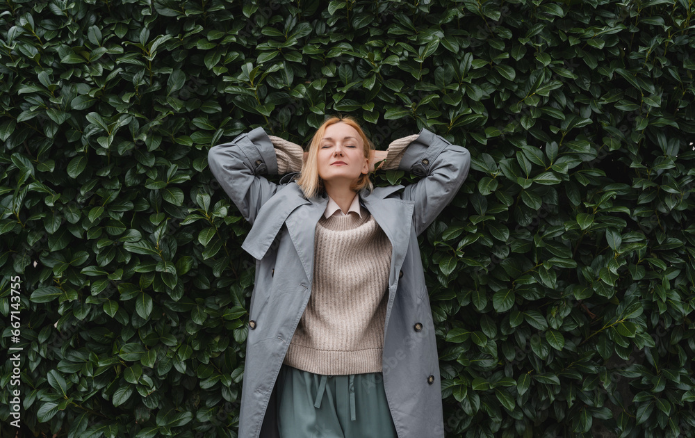 Woman with eyes closed on background of green leaves wall. Concept of outside of office, Work-Life-Balance, Taking Break.