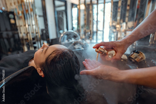 Professional stylist worker or hairdresser is washing customer hair with shampoo and water at professional sink in beauty salon or barber shop. Hair care concept.