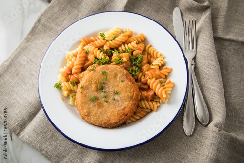 Jägerschnitzel nach DDR Rezept mit Jagdwurst paniert, Spirelli Fusilli Nudeln, Tomatensoße, Petersilie auf Emaille Teller, Besteck und grauer Leinen Serviette