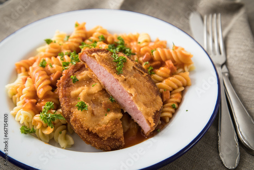 Jägerschnitzel nach DDR GDR Rezept mit Jagdwurst paniert, Spirelli Fusilli Nudeln, Tomatensoße, Petersilie auf Emaille Teller, Besteck und grauer Leinen Serviette