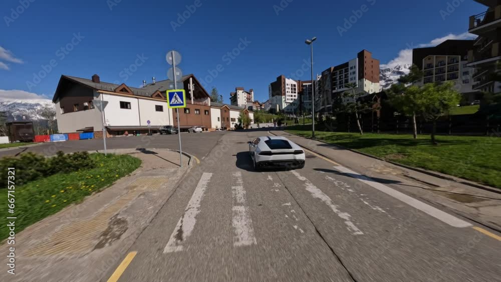 Aerial follow view white speed sports car riding asphalt road suburb alpine resort street infrastructure mountain sunny snowy peak. FPV drone shot traffic roadway town landmark village house exterior Aerial follow view white speed sports car riding asphalt road suburb alpine resort street infrastructure mountain sunny snowy peak. FPV drone shot traffic roadway town landmark village house exterior