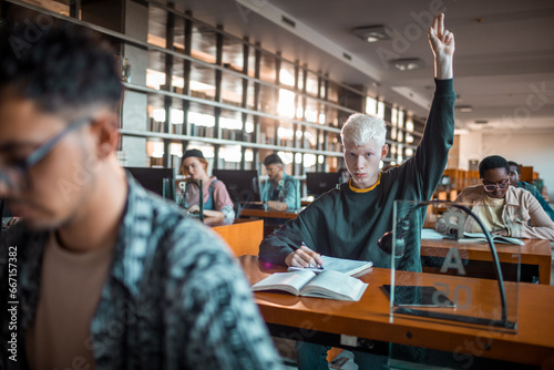 Young male student raising his hand to ask a question during lecture in the library