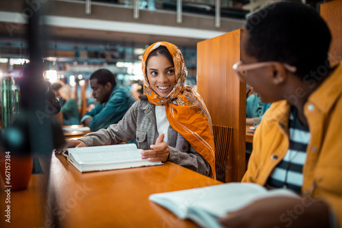 Young Muslim woman talking to a friend in a university library photo