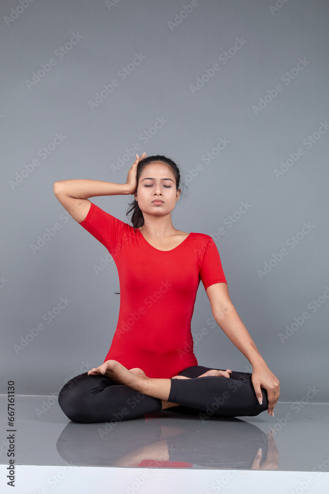 Fototapeta premium Healthy young woman in red t-shirt and black leggings doing yoga and stretching exercises isolated on grey background