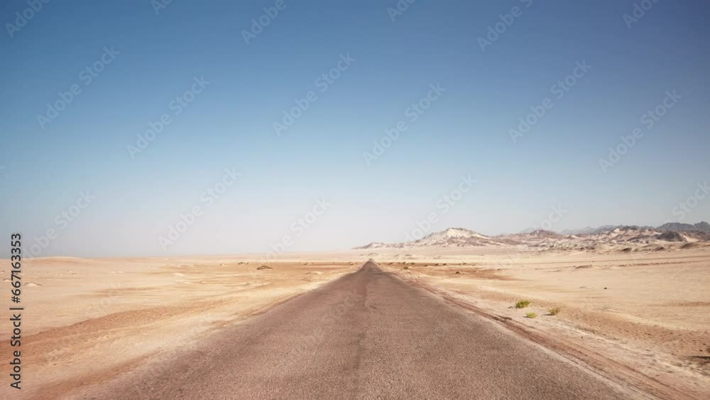 First person view of motion by empty road through the wild desert. Clear blue sky and mountains on the horizon First person view of motion by empty road through the wild desert. Clear blue sky and mountains on the horizon