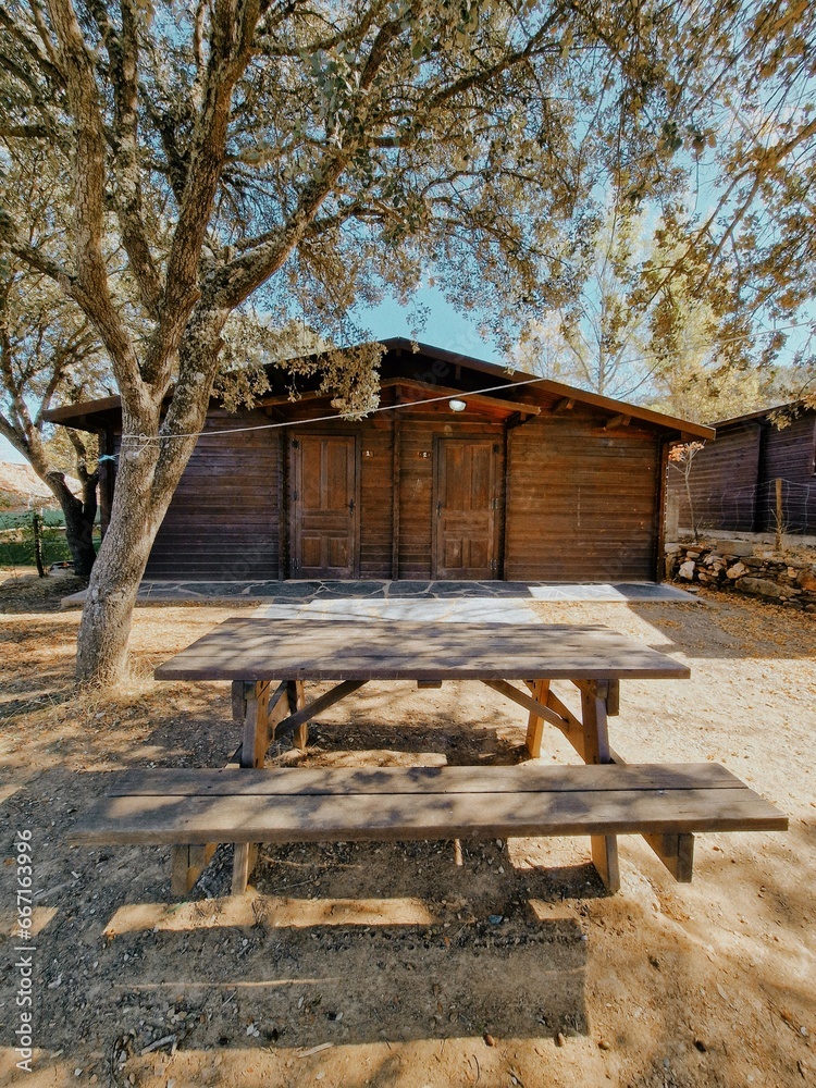 Wooden bungalow on a campsite along with a table and benches for a nice picnic under the warm sun