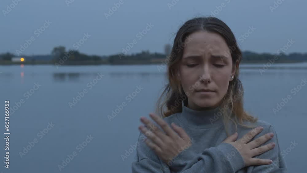 Female tapping her shoulders outdoors near water. Crossing hands
