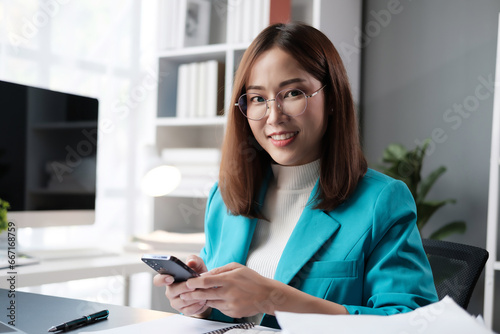 Happy young Asian business woman with a smile using smartphone at the office.