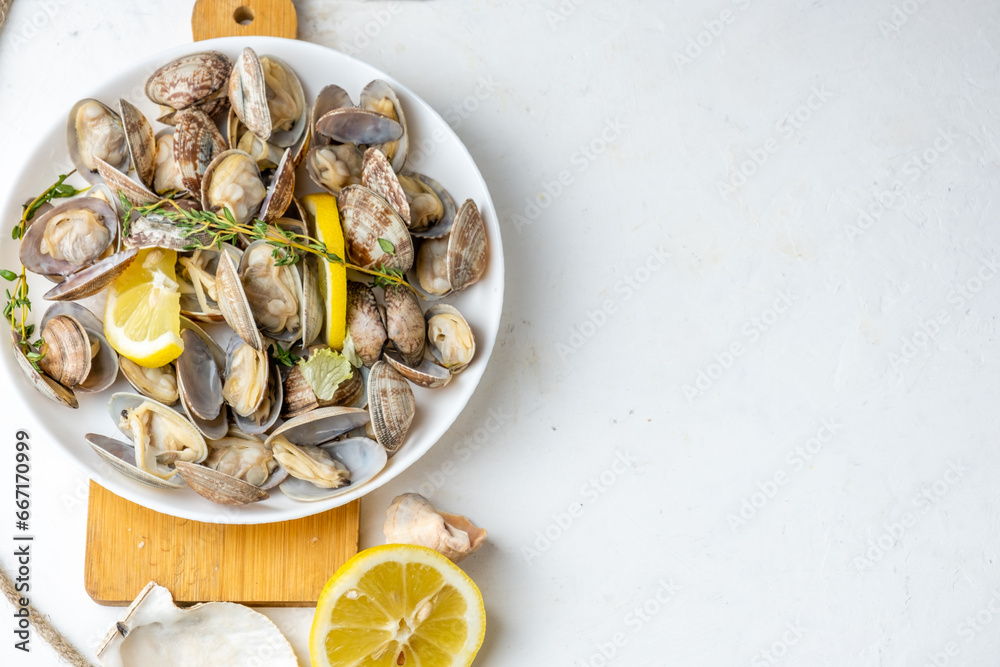 appetizer of steamed vongole clams, served in a white plate with lemon and herbs, top view, free space on the right. appetizer of steamed vongole clams, served in a white plate with lemon and herbs, top view, free space on the right.