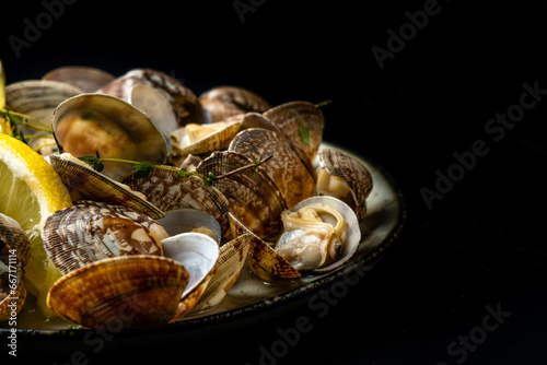 Vongole clams with lemon and herbs close-up in a plate, free space.
