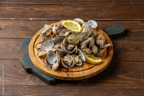 Vongole on a wooden tray served with lemon and herbs, wooden background.