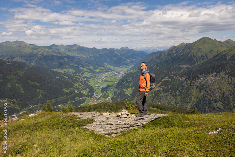Gray-haired man with backpack standing on mountain and looking at further route up, Austria