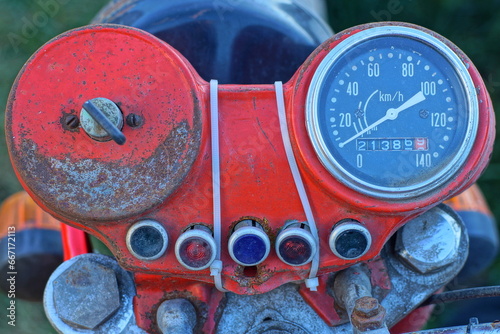 ront black  metal part with a glass black speedometer and a metal key in the ignition and a part of a chrome iron steering wheel with a headlight from an old retro red  motorcycle 
 photo