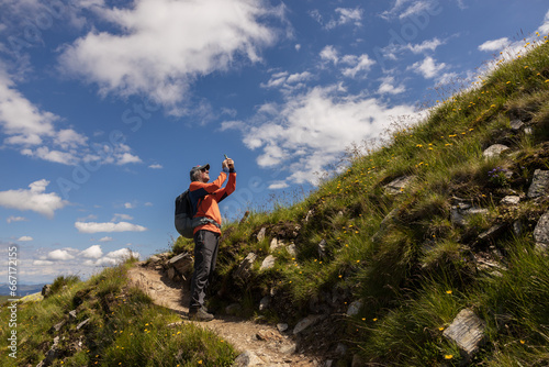 Man with backpack standing on trail with taking pictures of further route against the background of picturesque sky