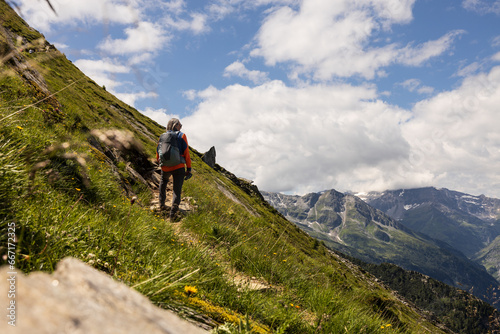 Gray-haired man with backpack climbing steep slope against bright sky and mountain range, Austria