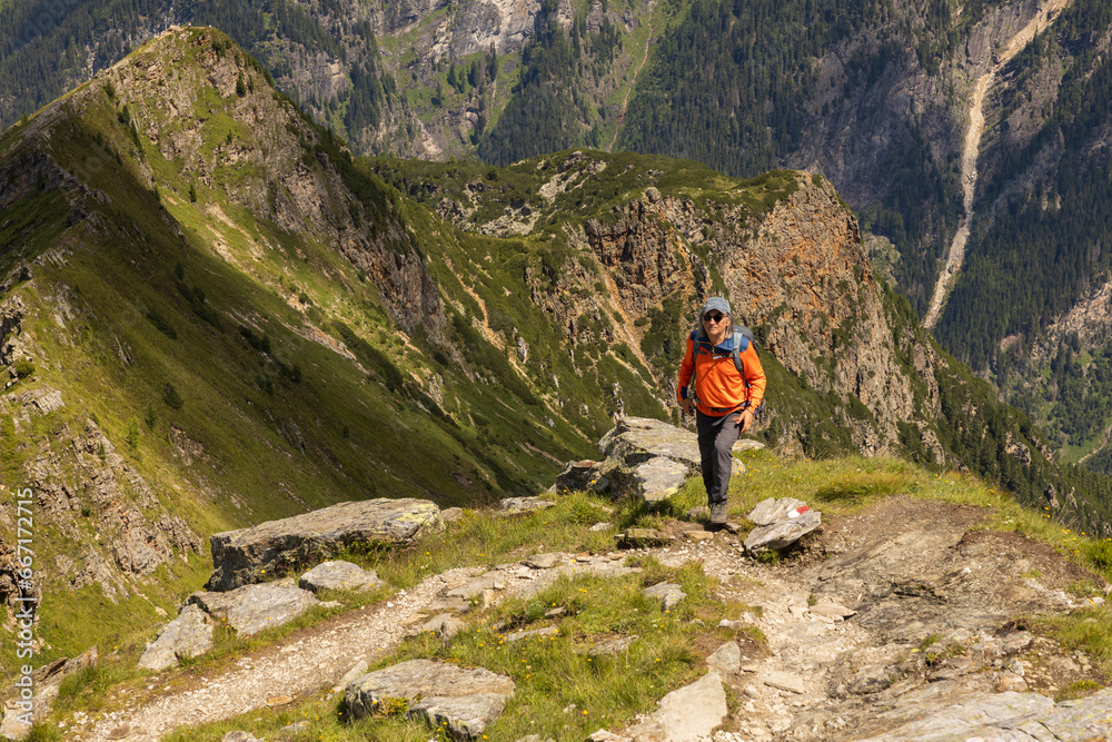 Adult man with backpack standing on steep rocky trail and looking at camera on background of alpine mountains, Austria
