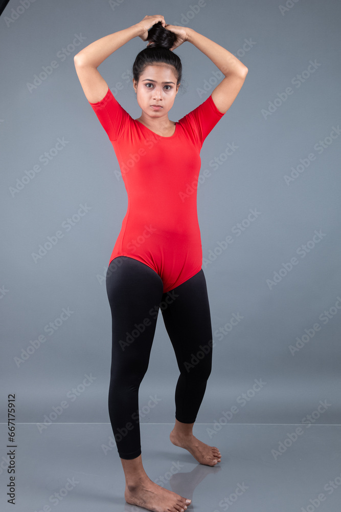 Healthy young woman in red t-shirt and black leggings doing yoga and stretching exercises isolated on grey background Healthy young woman in red t-shirt and black leggings doing yoga and stretching exercises isolated on grey background