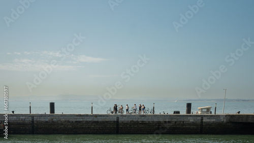 Lisbon, Portugal - May 25, 2023: Silhouettes of a group of bicycle riders by the Tagus river on a sunny day