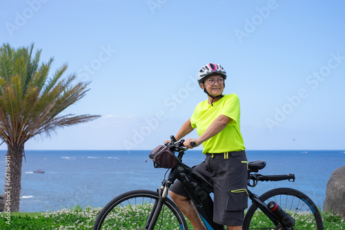 Elderly athletic woman with electric bicycle in outdoors excursion at sea. Senior woman in helmet enjoying freedom and healthy lifestyle