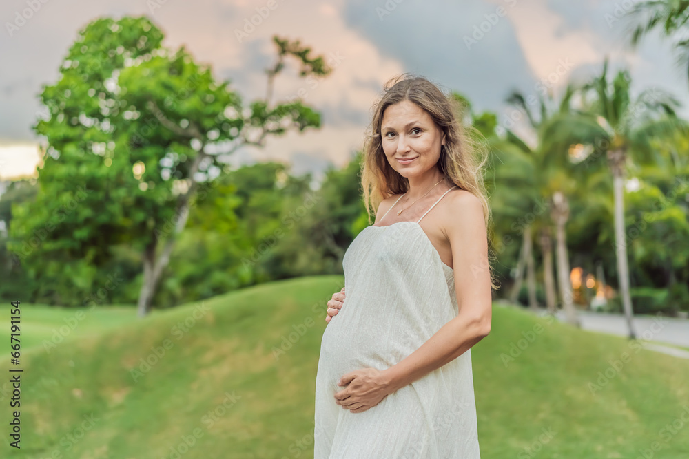 Pregnant woman hugging her tummy standing outdoors surrounded by nature. Pregnancy, expectation, motherhood concept Pregnant woman hugging her tummy standing outdoors surrounded by nature. Pregnancy, expectation, motherhood concept