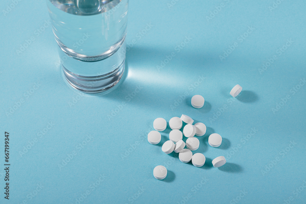 Herbal and Vitamin white pills healthy food freely laid near glass of water on light blue background for healthy eating in daily life