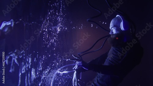 A young brutal man in a futuristic suit and headphones listens to music underwater.