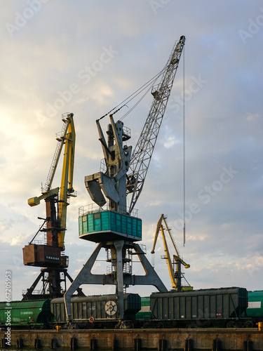 Harbor cranes with grain wagons between crane legs, seaport industry scene, grain export