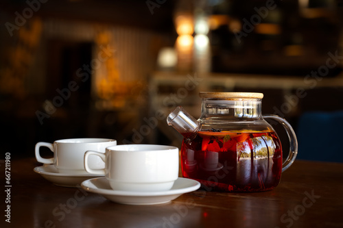 Black tea with fruit in two white tea cups and a glass teapot on a brown wooden stand. Black tea with oranges, cinnamon, cloves and sugar. Tea concept