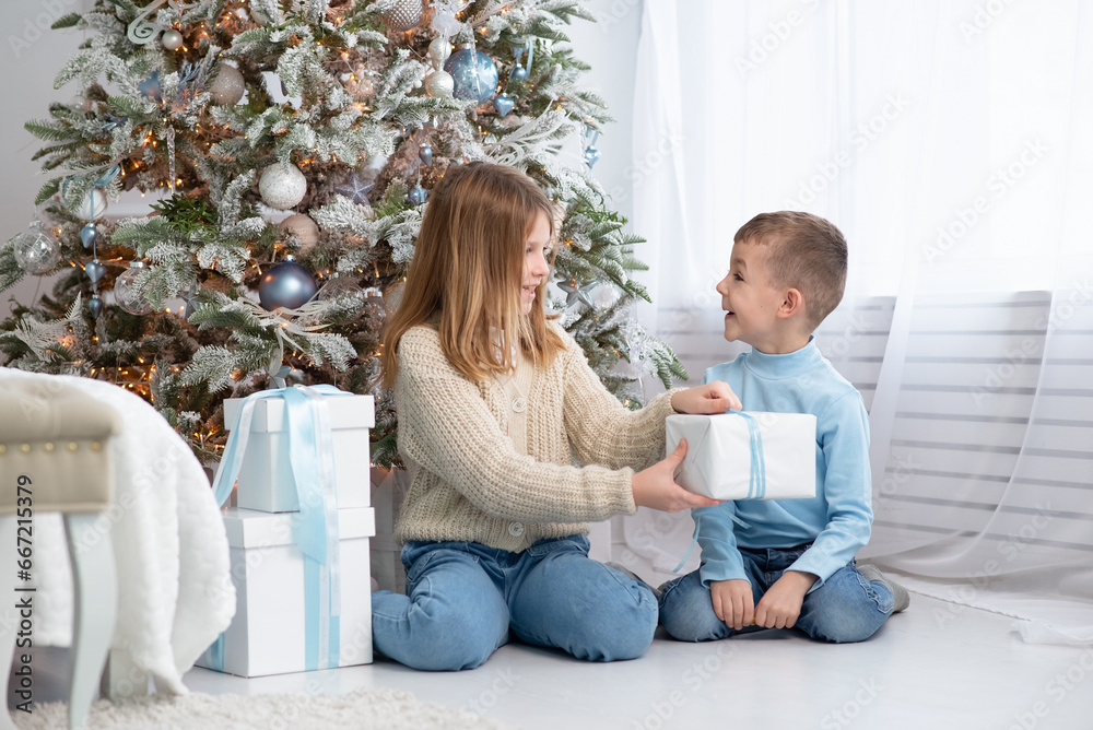 a boy and a girl give each other gifts against the background of a New Year tree. happy brother and sister opening New Year's gifts a boy and a girl give each other gifts against the background of a New Year tree. happy brother and sister opening New Year's gifts