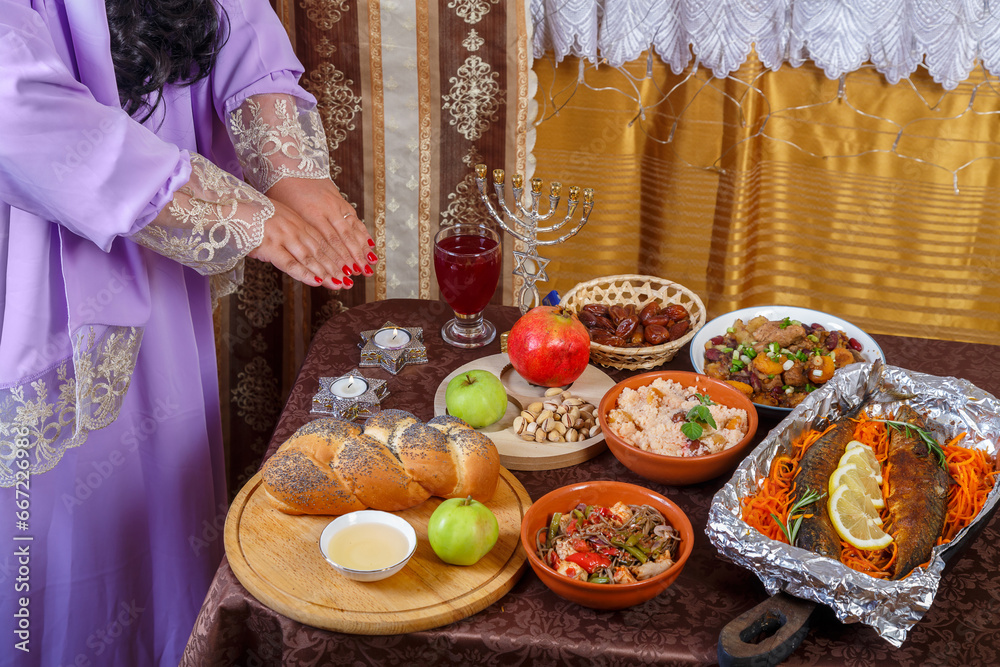 A Jewish woman reads a blessing on candles at a set table on the Jewish holiday of Rosh Hashanah