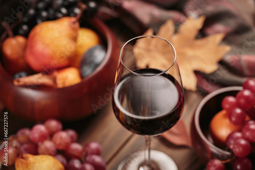 Glass of rich red wine served with fruits on dark wooden background. Autumn still life with wine, grapes and dry leaves in rustic style. Sweater weather concept