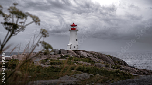 Photograph of a red and white lighthouse on a rock in the middle of nowhere. Grey and stormy weather 