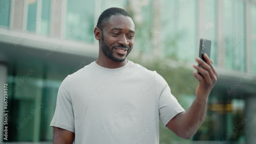 Charismatic positive african american man calling video chat on smartphone stand on city street looking at screen. Portrait smiling friendly guy talking on mobile phone. Online conversation concept. Charismatic positive african american man calling video chat on smartphone stand on city street looking at screen. Portrait smiling friendly guy talking on mobile phone. Online conversation concept.