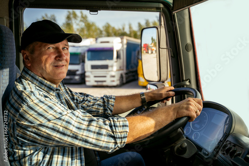 Positive Caucasian middle age trucker sitting in front of wheel and looking at camera  photo