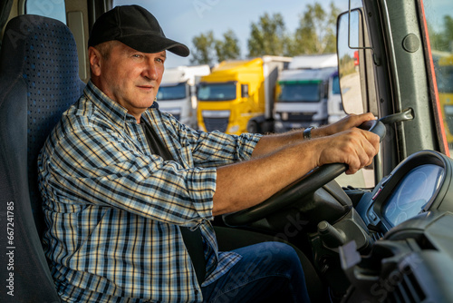 Closeup shot, amazing lighting, trucker sitting in front of wheel ready to start his day, parked trucks in the back 