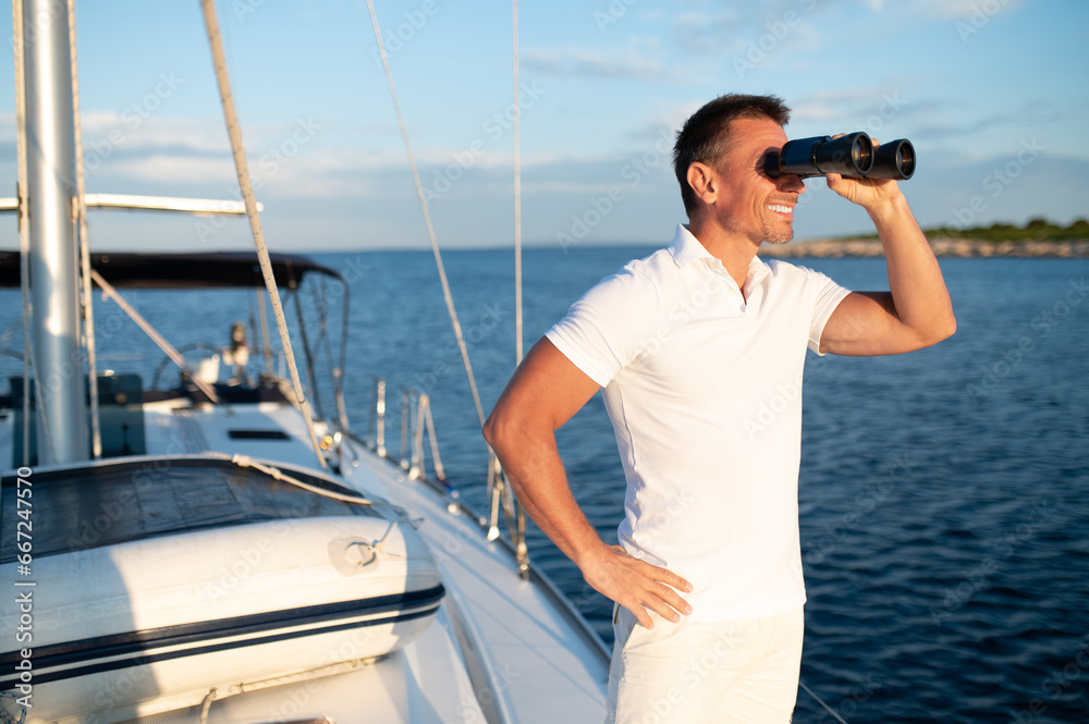 Obraz premium Man with binocular standing on a yacht deck