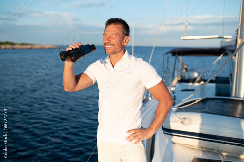 Smiling man in white with binocular standing on the yacht