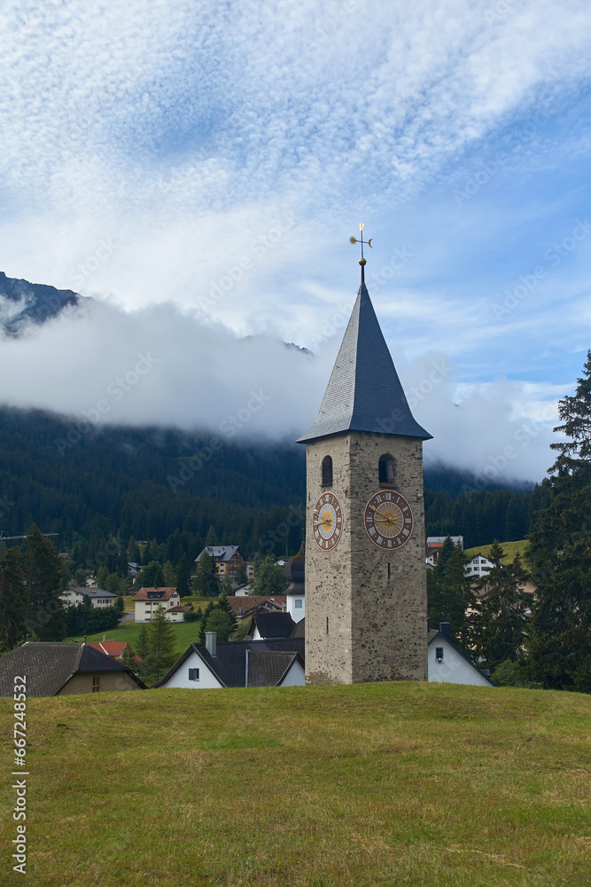 Beautiful swiss alpine countryside with a medieval bell tower with a clock and Rothorn mountain on background in Churwalden village in Switzerland formerly Parpan