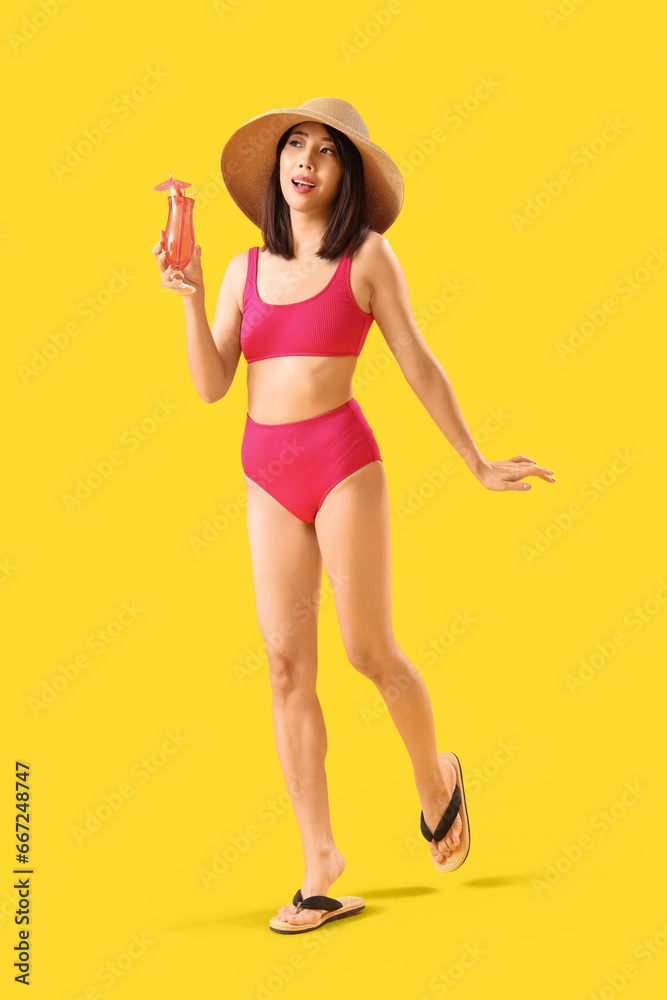 Beautiful Asian woman in swimsuit and with cocktail on yellow background Beautiful Asian woman in swimsuit and with cocktail on yellow background