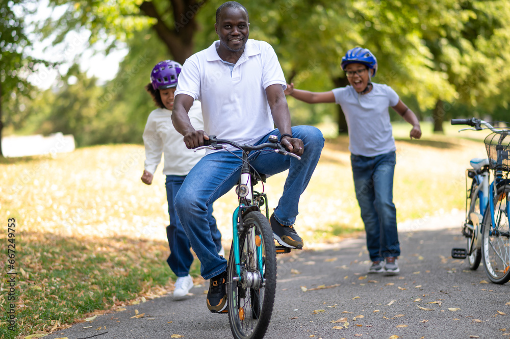 Obraz premium Happy family riding a bike in a park and having fun together