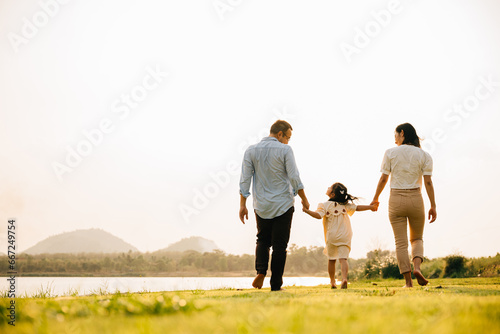 Asian father and daughter walking hand in hand in a scenic garden on a sunny day, enjoying quality time together and the beauty of nature, Family day, back view