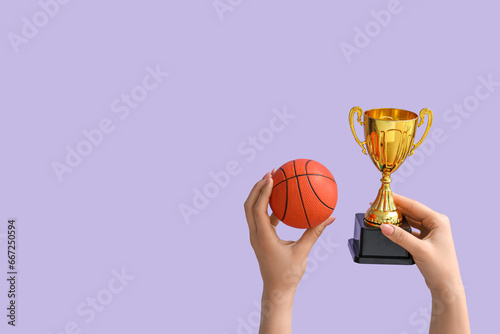 Female hands with gold cup and basketball on lilac background © Pixel-Shot